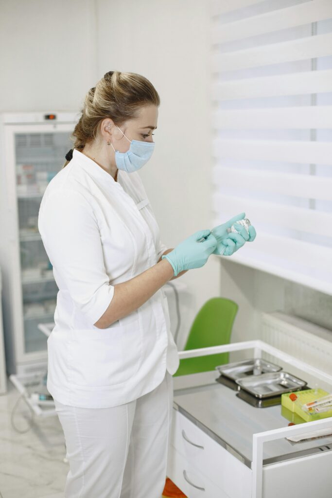 A female doctor in a clinic holding a medicine vial while wearing gloves and a mask. Perfect for healthcare themes.