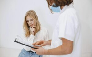 A doctor in a face mask discusses diagnosis with a patient in a clinic setting.