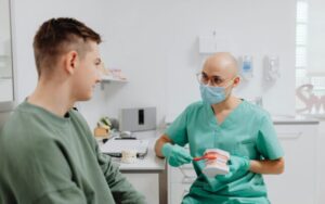 A dentist in scrubs teaches a young man oral hygiene using a dental model in a bright clinic.